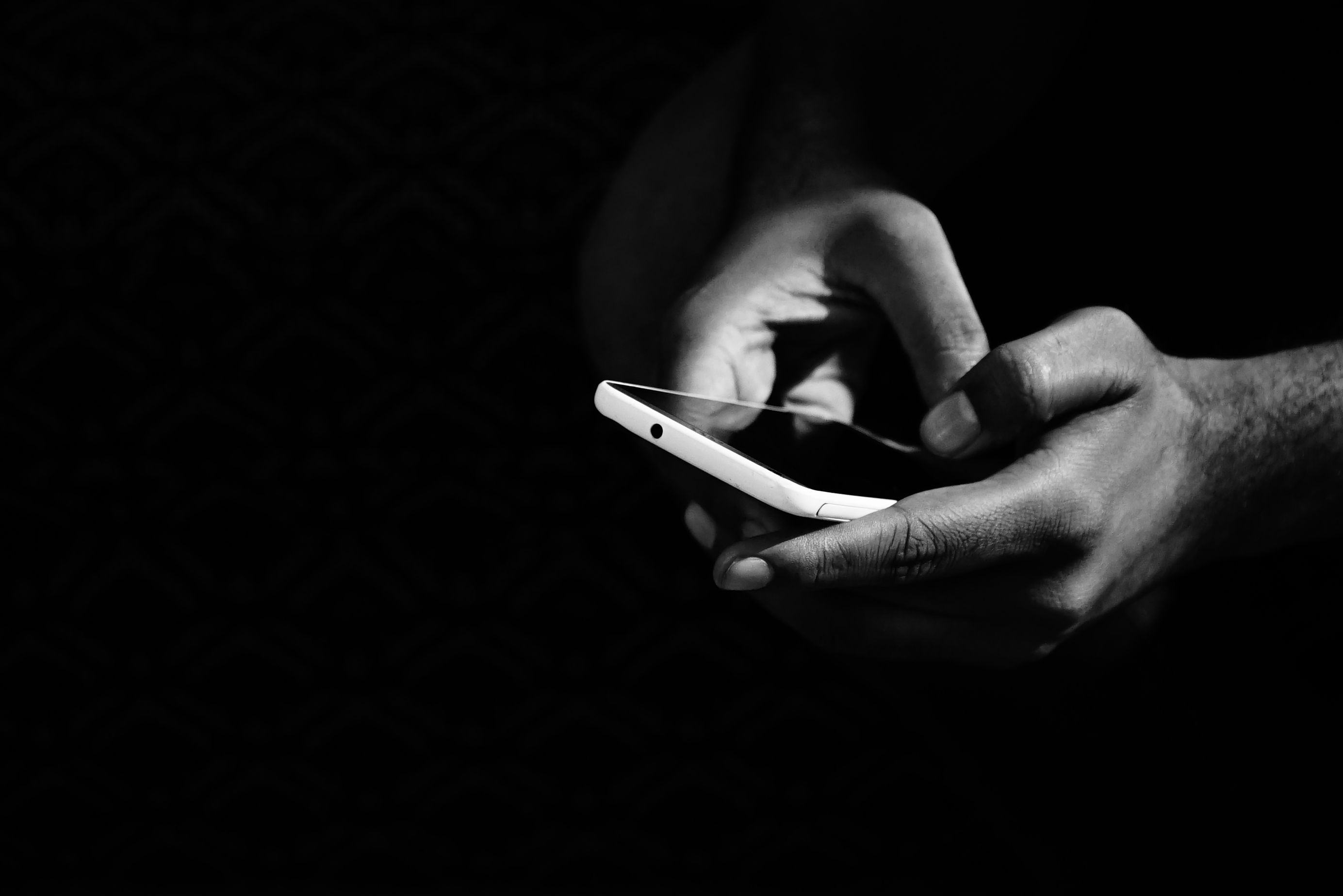 Manos usando un teléfono móvil, en una fotografía en blanco y negro.